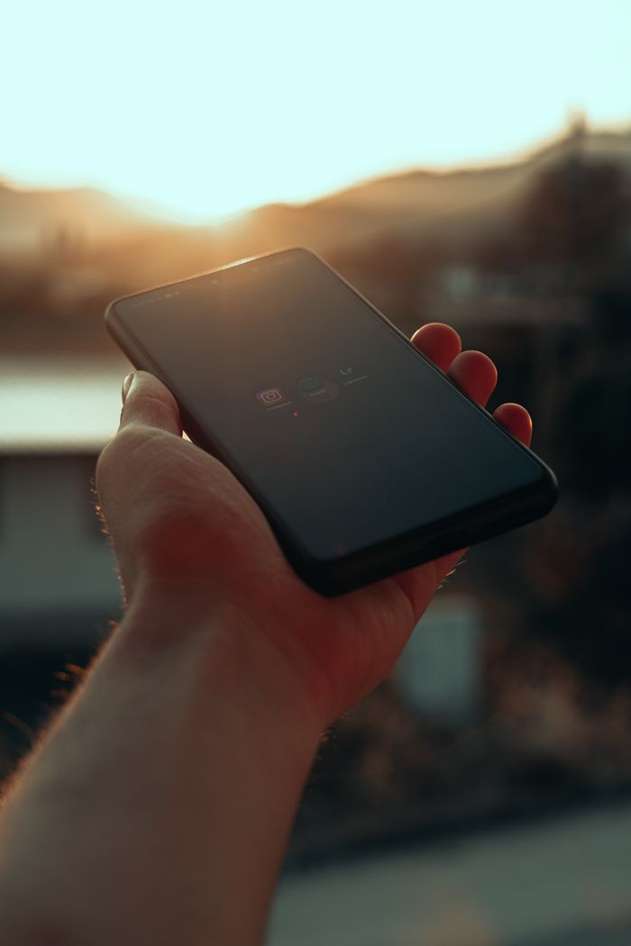 Close-up of a hand holding a smartphone against a sunset backdrop, capturing a serene moment.