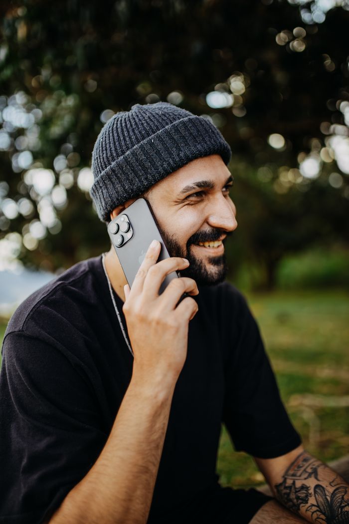 our-story-02 Smiling man with beard and knit hat talking on smartphone outdoors in a park.
