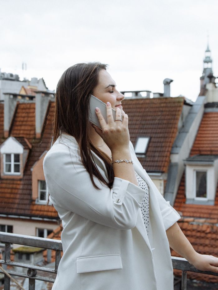 why-choose-us-02 Businesswoman in a white suit talking on phone, standing outdoors against an urban rooftop backdrop.